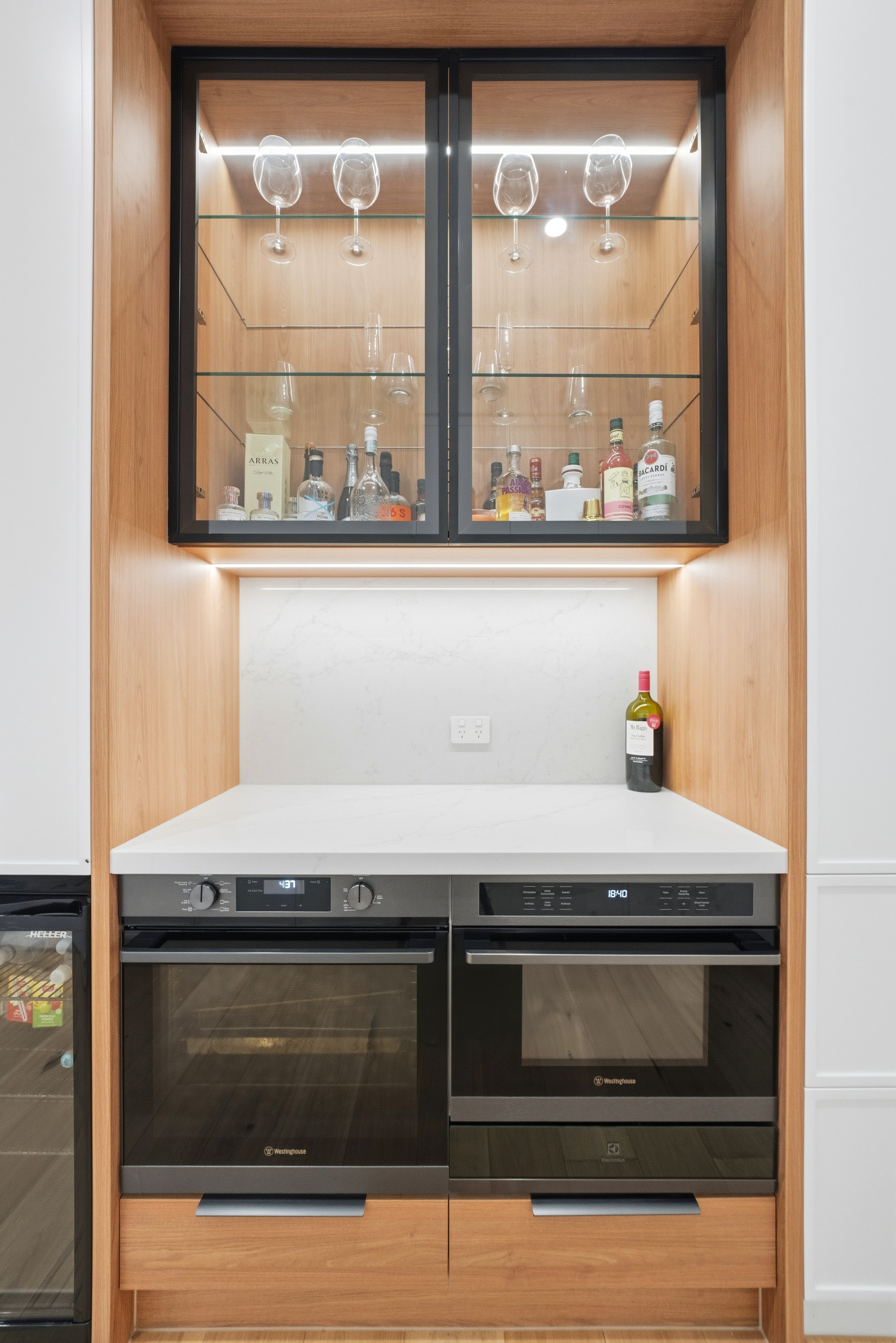 Bar nook with lit glass cabinetry and double wall ovens